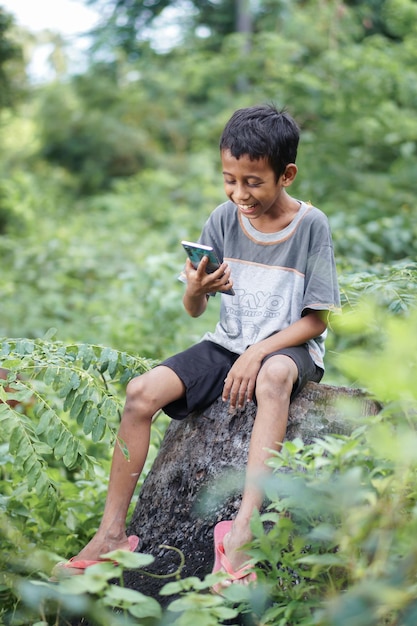 A boy sits on a rock and reads a message on his phone.