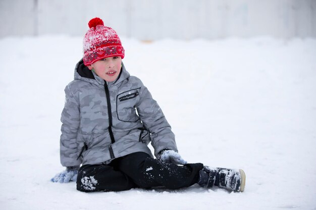 The boy sits in the snow in winter