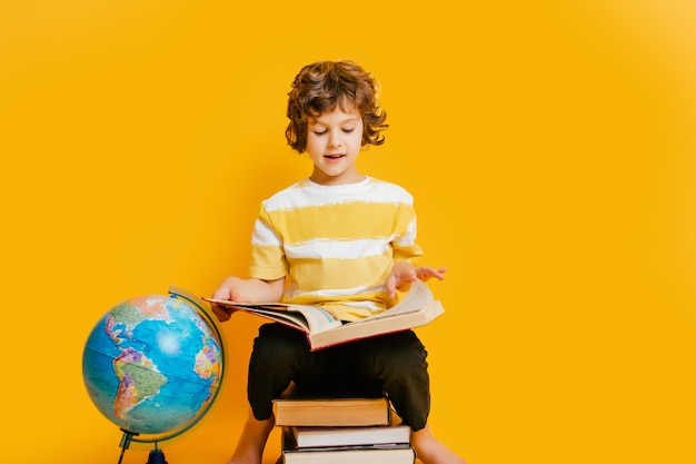 boy sits on a stack of books, near to the globus