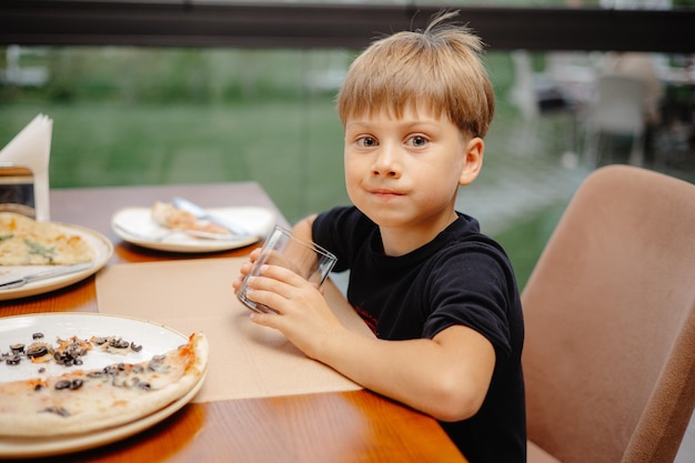 ピザのプレートとコップ一杯の水を持ってテーブルに座っている男の子。