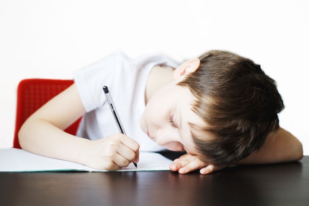 The boy sits at the table and writes in a notebook