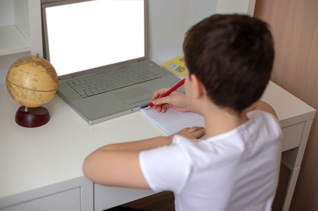 boy sits with his back behind a laptop, looks at the monitor.
