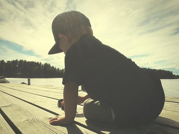 Photo boy sitting by lake against sky