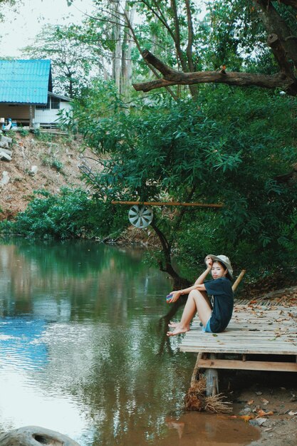 Foto ragazzo seduto vicino al lago contro gli alberi