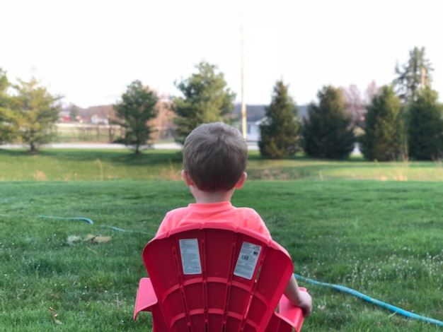 Boy sitting on chair in grass