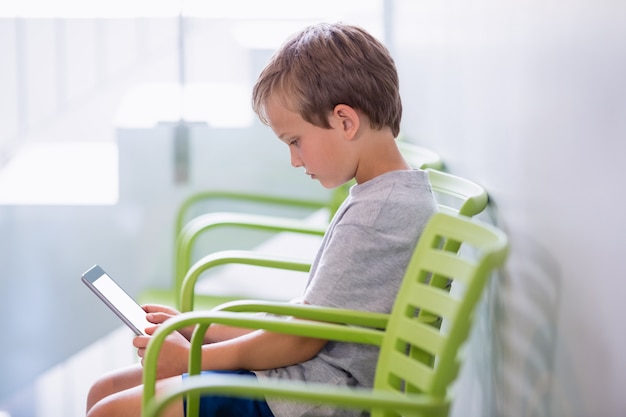 Мальчик сидит на стуле с помощью цифрового планшета в коридоре