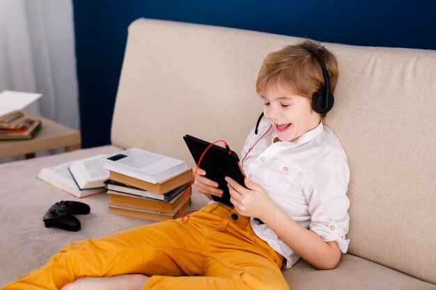 Boy sitting on the couch, eating pop corn and playing with gamepad during his online lesson at home, social distance during quarantine, self-isolation, online education concept