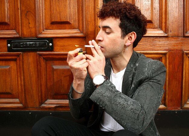 boy sitting in door lights cigarette