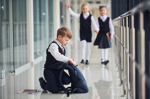 床に座っている男の子廊下で一緒に制服を着た学校の子供たち