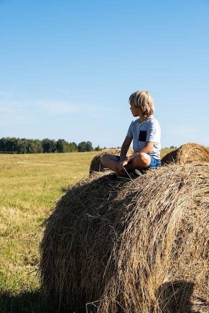 Foto ragazzo seduto sul pagliaio estate in campagna