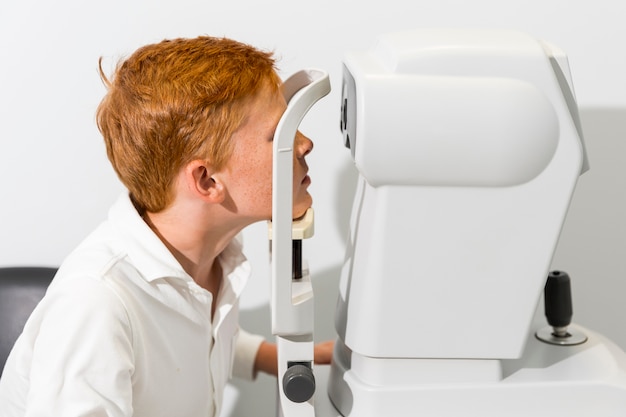 Boy sitting and looking at refractometer eye test machine at optician