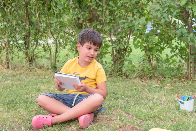 Boy sitting and relaxing on a hill reading a book in a meadow concept for education and relaxing