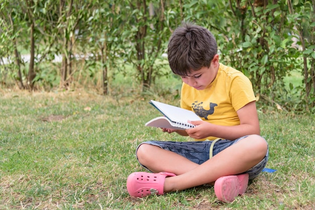 Boy sitting and relaxing on a hill reading a book in a meadow concept for education and relaxing