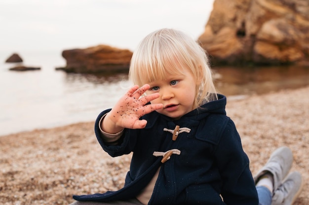 Boy sitting on the sandy beach near sea in autumn or summer time