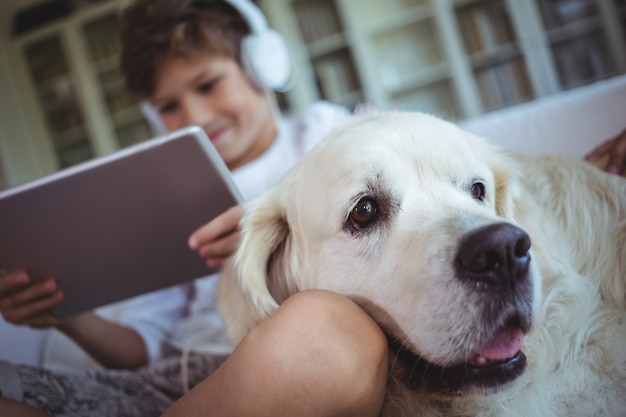 Photo boy sitting on sofa with pet dog and listening to music on digital tablet