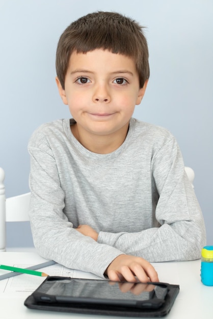 A boy sitting at the table with tablet and studing