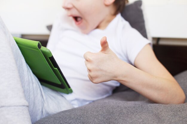 Boy sitting with a tablet on the bed in the room