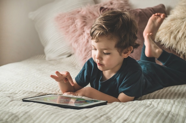 ベッドの上にタブレットを持って座っている少年