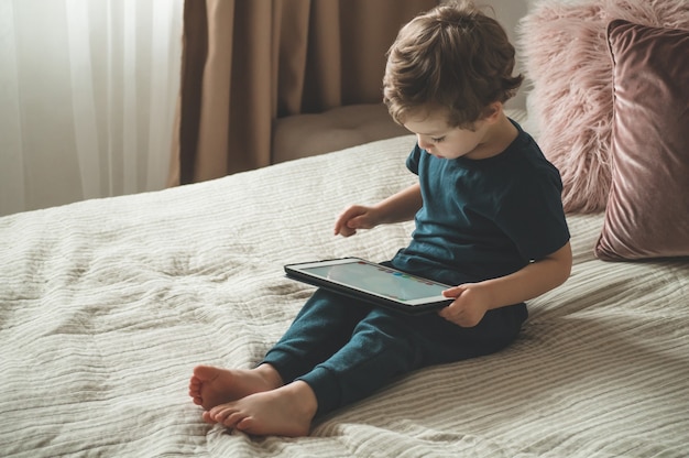 Boy sitting with a tablet on the bed