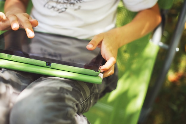 庭でタブレットを持って座っている少年