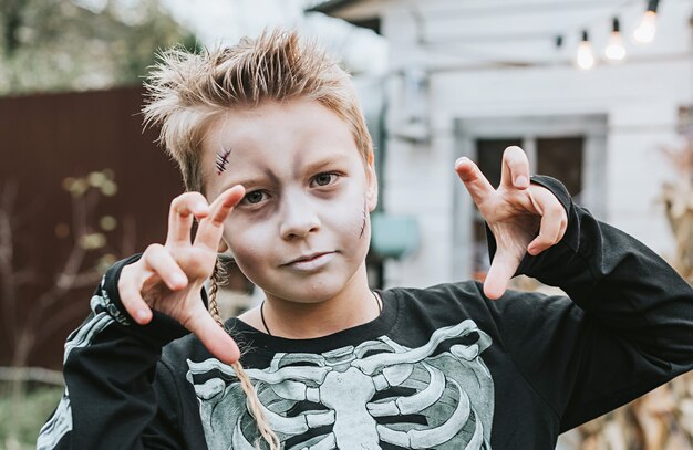 A boy in a skeleton costume with a painted face on the porch of a house decorated to celebrate a Halloween party