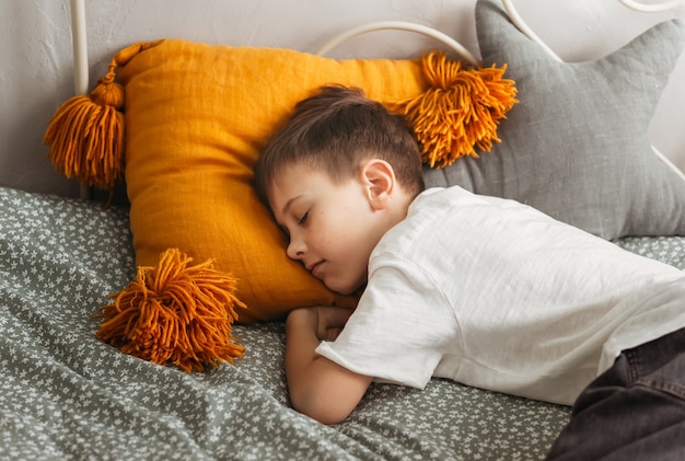 The boy sleeps on a pillow on the bed during the day. Daytime sleep