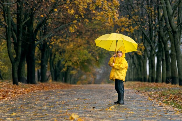 Photo boy smiling with large yellow umbrella in hands in the autumn park rainy fall day