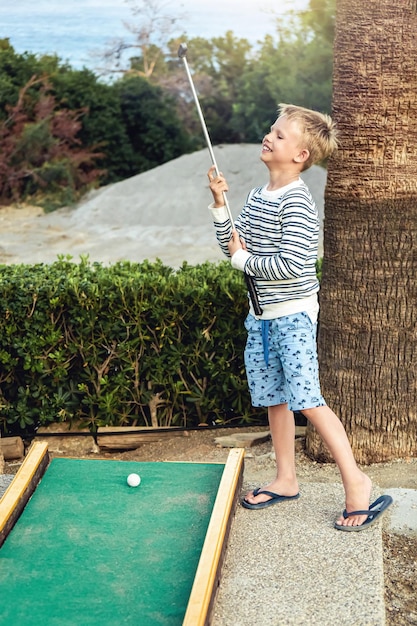 Boy speelt enthousiast minigolf op zomeravond op het grondgebied van het hotel