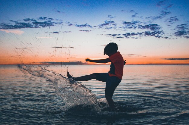 Foto ragazzo che spruzza acqua in mare contro il cielo durante il tramonto
