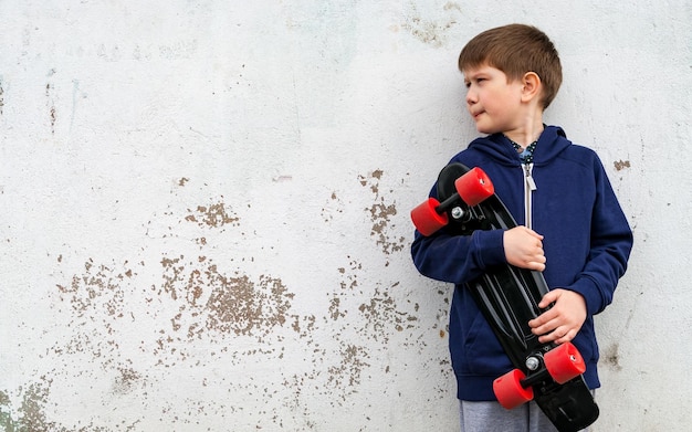 Foto un ragazzo in abiti sportivi con un pattino sullo sfondo di una parete intonacata
