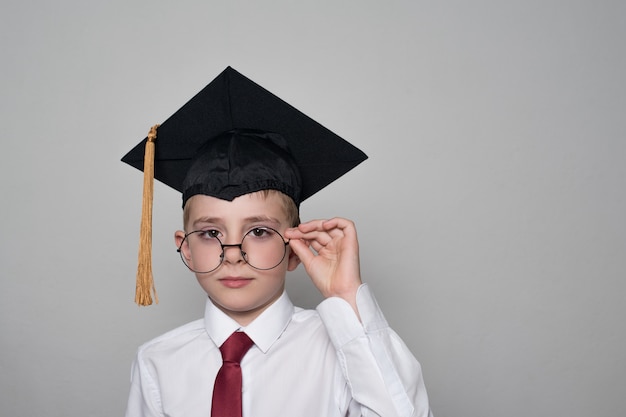 Boy in a square academic cap and white shirt correcting glasses