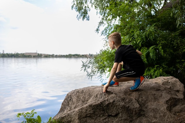 The boy squatted down on a large rock and looked at the river