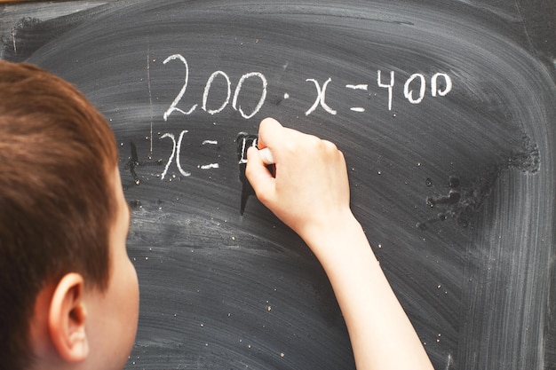 Boy standing back in front of a school blackboard and writing