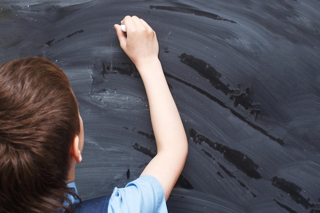 写真 学校の黒板の前に立って書いている少年