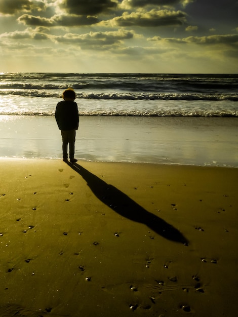 Foto ragazzo in piedi sulla spiaggia durante il tramonto