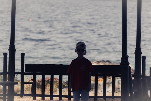 Foto ragazzo in piedi vicino alla recinzione contro il mare