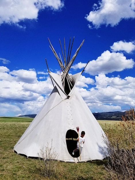 Boy standing by tent on landscape against sky