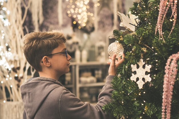 Photo boy standing by tree while touching christmas decoration at home