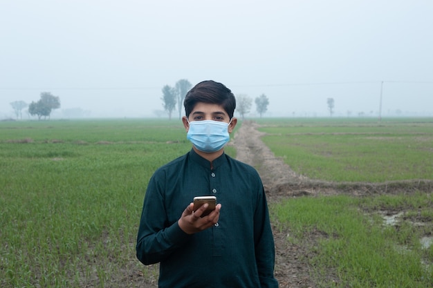 boy standing at the field wearing mask and mobile in hand