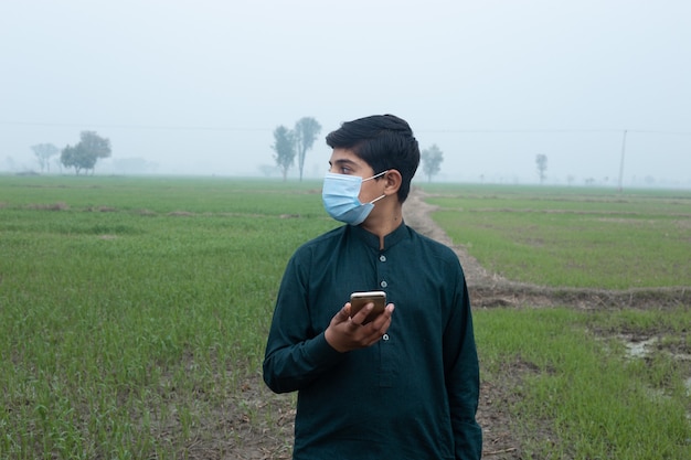 boy standing at the field wearing mask and mobile in hand