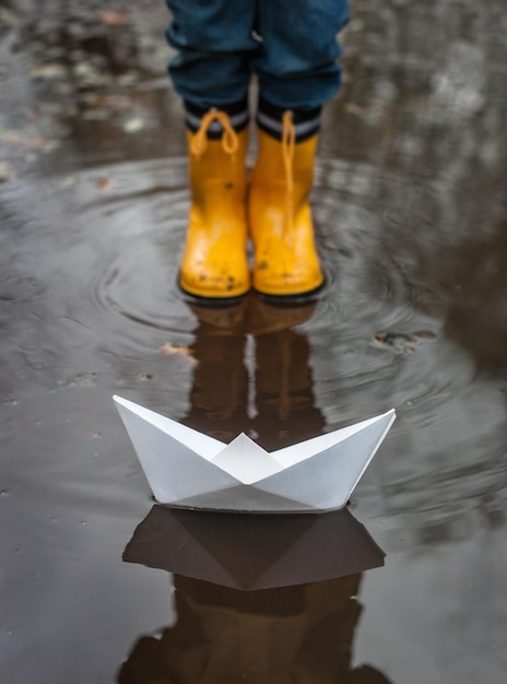 Photo boy standing in front of paper boat in puddle