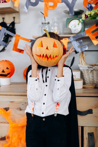 Boy standing  in masquerade  dress holding a pumpkin and hide his face Vertical 