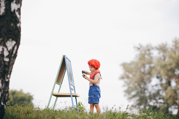 ツリーの下に立って、公園でイーゼルに描く少年