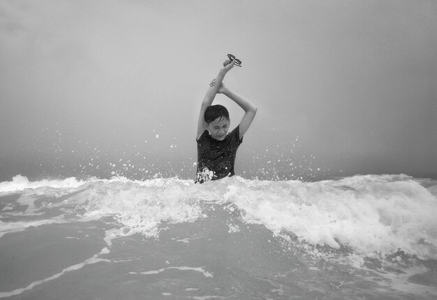 Photo boy standing with arms raised in sea against sky