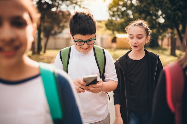 校庭でスマートフォンを使用して友人と立っている少年