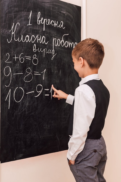 A boy stands at the blackboard and solves a math example