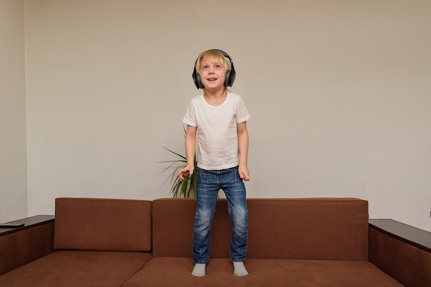 Boy stands on couch in headphones. Child listens to music and dances