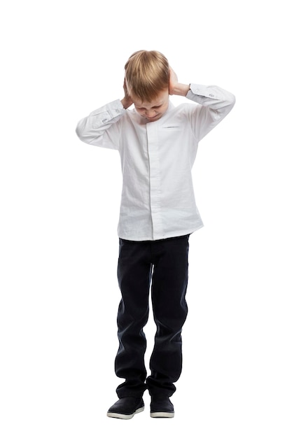 The boy stands and holds his head with his hands. Stress and negative emotions. A guy in a white shirt and dark trousers. Isolated on white background. Vertical.