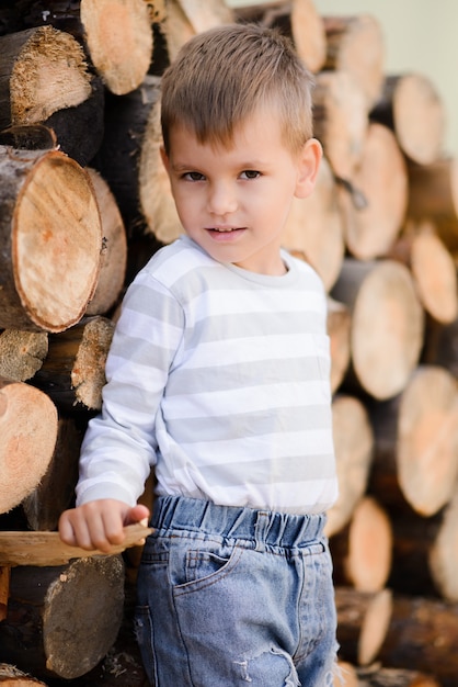The boy stands near the wooden logs and smiles looking at the camera