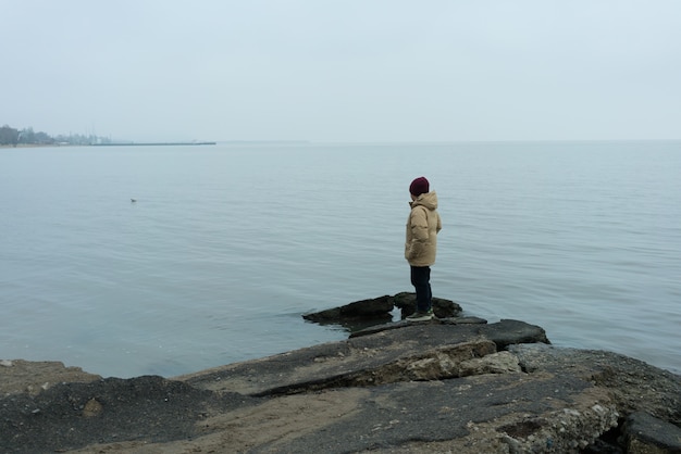 A boy stands on a rock in the black sea and looks out at the water